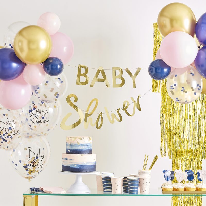 Dekoration Baby Shower in gold, rosa und blau. Auf dem Tisch steht eine Babytorte und Pappbecher, sowie Teller in blau und rosa Gender Revael Party