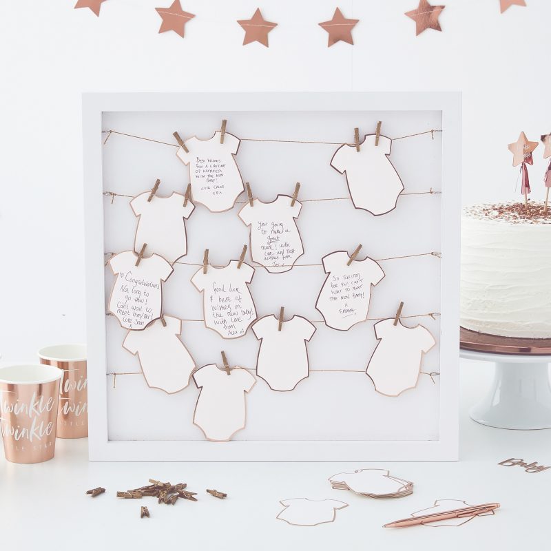 Weißer Rahmen mit 25 Babybodys aus Papier, um Wünsche für das Baby festzuhalten. Die Babybodys sind mit kleine Wäscheklammern im Rahmen befestigt.